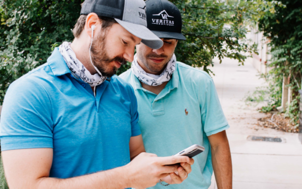Two contractors use a software on their mobile phone while outside