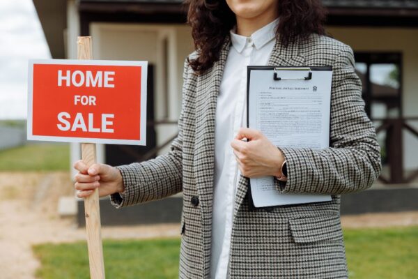 Realtor holding mortgage papers and a for sale sign