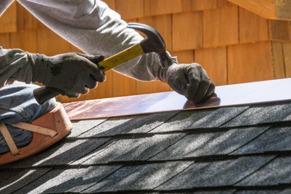 roofer wearing gloves while hammering a roof